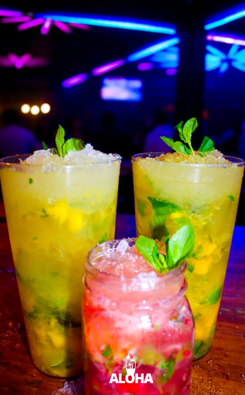 Trío de litros y mason jar en barra Aloha con gente al fondo